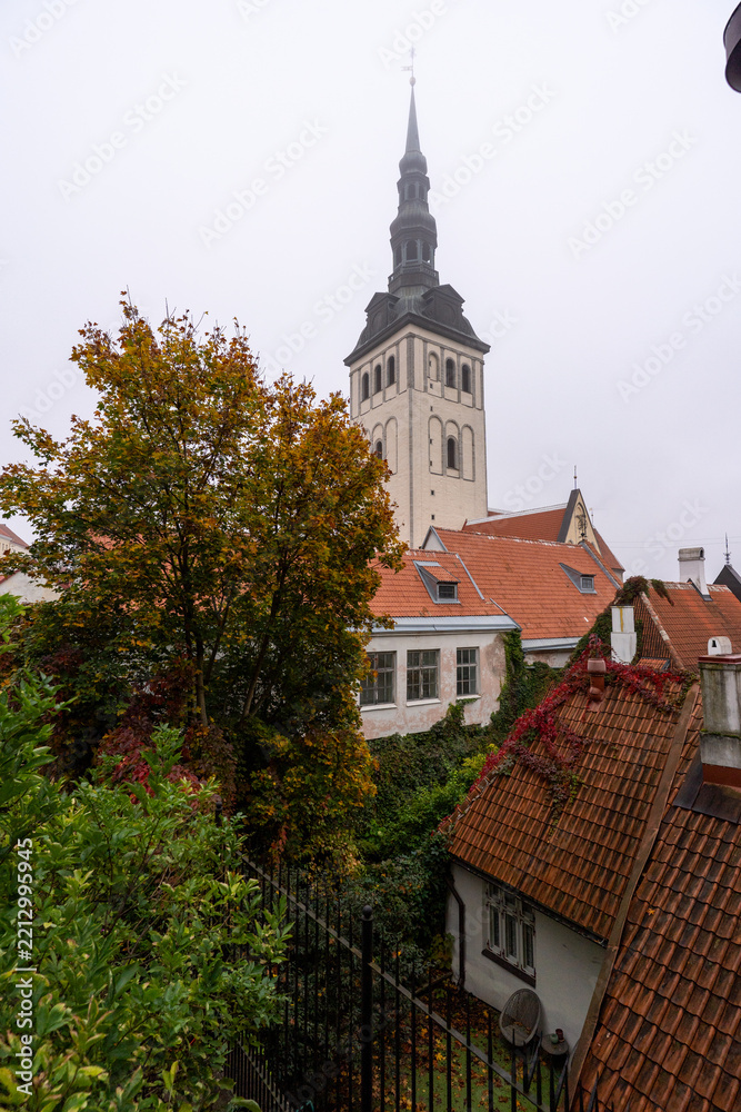 Fototapeta premium Tallinn, Estonia - October 2, 2026: A church tower above red tiled roofs and autumn foliage in Tallinn Old Town.