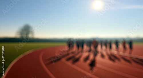 Blurred figures on a track, casting long shadows under a bright sun