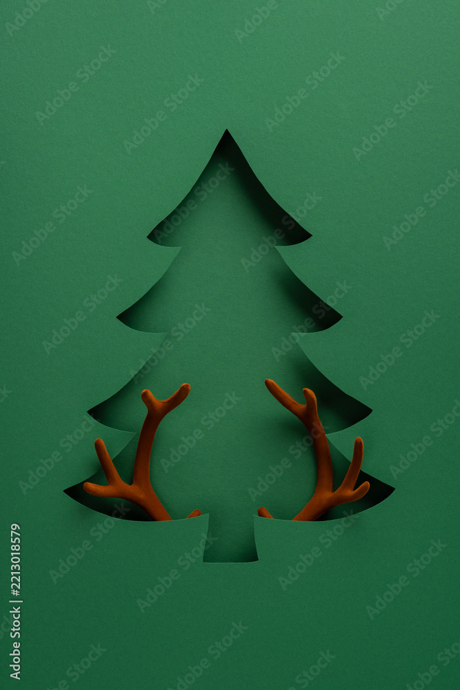 Fototapeta premium Merry Christmas and Happy New Year paper cut tree with reindeer antlers minimalist vertical green holiday design
