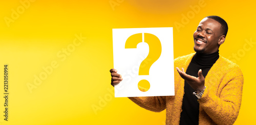 Obraz na plátně Smiling man holding a large question mark sign against a vibrant yellow backgrou