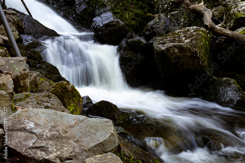 Flowing water spills across uneven rocks covered with green moss and surrounded by dense vegetation in a natural forest setting