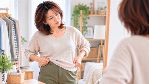 鏡を見ながら服の似合い方を確認する中年女性