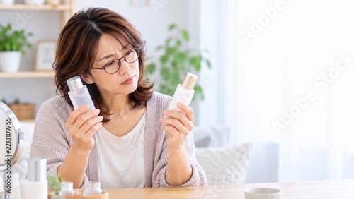 老眼鏡をかけて化粧品を比較する中年女性