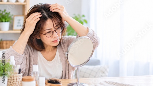 鏡を見ながら髪の分け目と頭皮を確認する中年女性