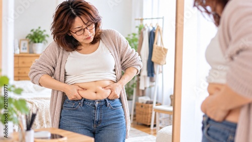 鏡の前でお腹とウエストの変化を確認する中年女性