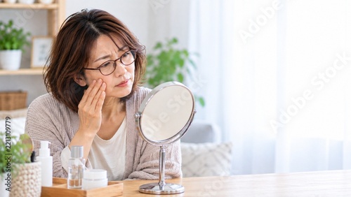 鏡を見ながら頬の肌状態を確認する中年女性