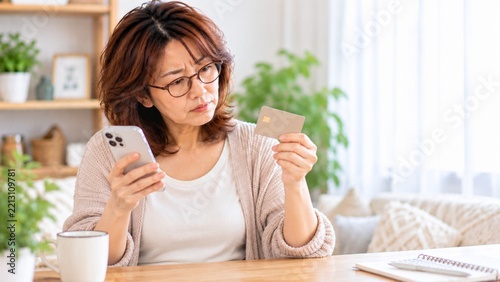 スマートフォンを見ながら支払いカードを確認する中年女性