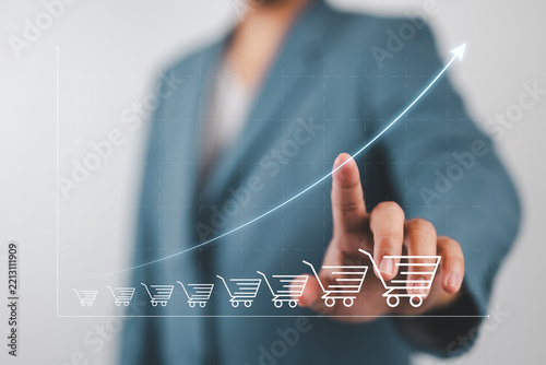 Businessman drawing increasing trend graph of sale volume with bigger shopping trolley cart for  online sale business growth concept.