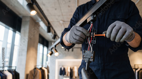 Electrician installing track lighting system in a modern retail clothing store interior