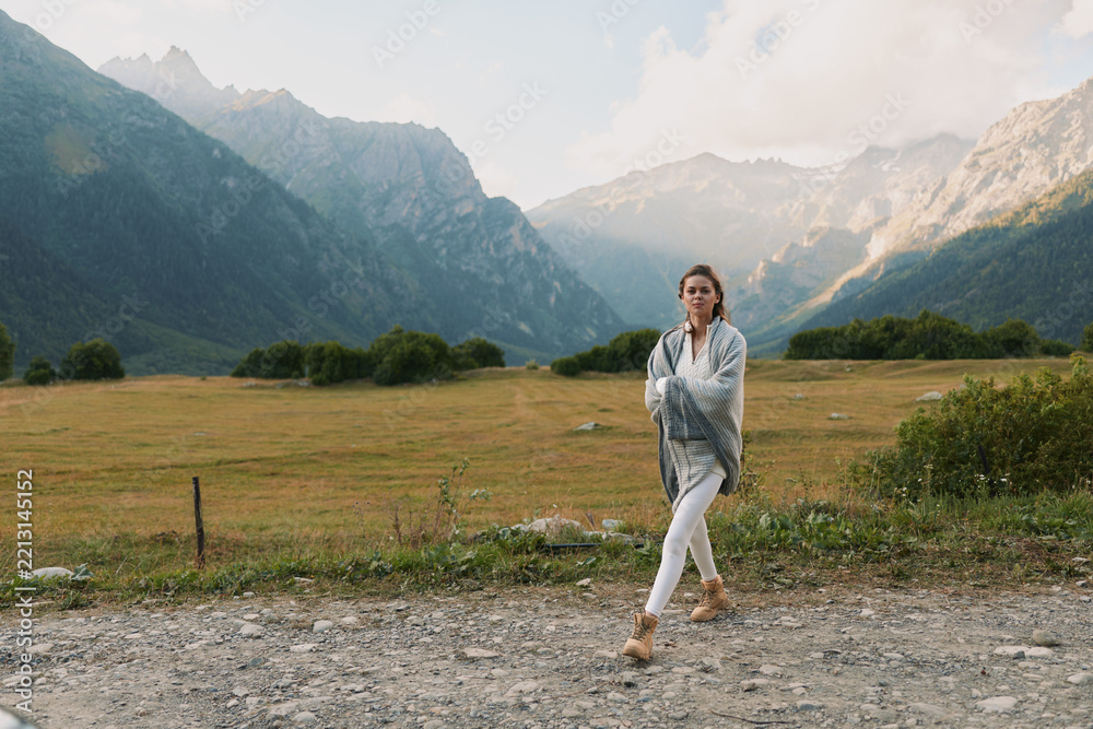 Obraz premium Young woman walks along a gravel road in a mountain valley, calm and thoughtful, framed by distant peaks, that suggest solitude, exploration, and a sense of open space.