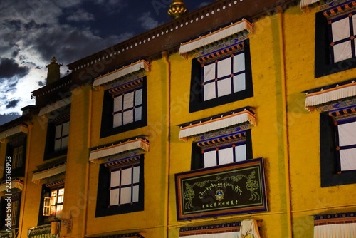 Yellow traditional Tibetan buildings with white-framed windows and ornate awnings glow at dusk on Barkhor Street, a historic area of Lhasa, Tibet, China.