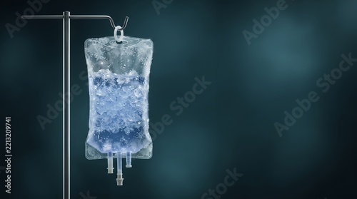 A solitary intravenous bag containing ice and blue liquid is suspended from a metal pole against a dark, moody background.