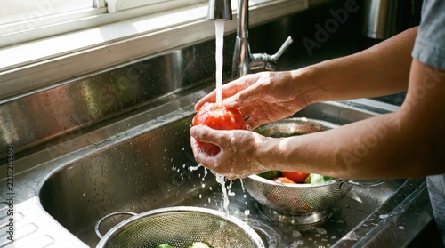Person washing fresh red tomatoes in a modern kitchen sink