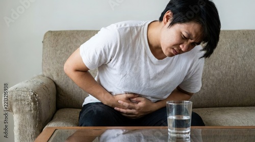 Young man suffering from stomach pain sitting on a sofa