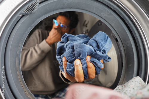 Man Holding Smelly Laundry In Front-Load Washing Machine While Reacting To Bad Odor