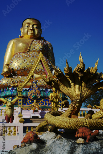 A large brilliantly gold-colored statue of Phra Maha Kaccayana Thera, holding a holy water vessel representing the 76 provinces standing 20 meters at Wat Lang San Prasit.