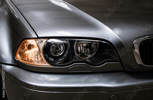 Close-up shot of a grey modern sedan car headlight with glowing amber signal light, representing luxury vehicle design, automotive lighting, German car engineering, and auto detail.