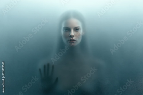 Mysterious woman behind frosted glass portrait with moody atmosphere