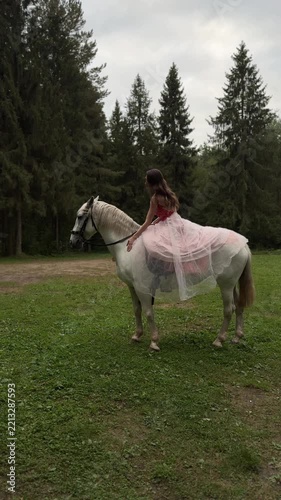 Model in a pink gown stroking a white horse from the saddle