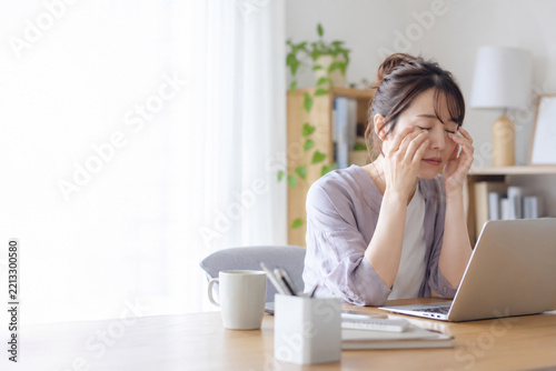 自宅でパソコン作業中に目をこすって疲れを感じる女性