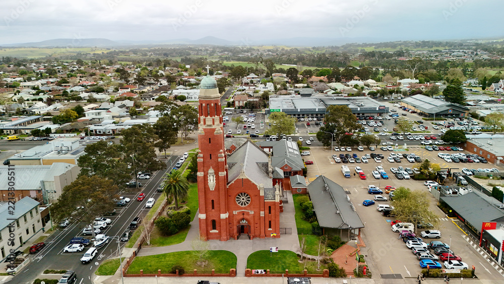 Fototapeta premium Bairnsdale, Victoria, Australia – 4K aerial drone view of regional city centre, St Mary’s Catholic Church, Main Street, roundabouts, residential areas and East Gippsland countryside