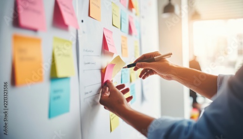 Hands adding colorful sticky notes to a wall for project planning and brainstorming. Team collaboration concept for creative ideas.
