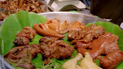 Various braised pork offal arranged on a fresh lotus leaf in a metal tray, displayed as market food.