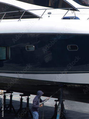 Worker Power Washing Yacht Hull in Dry Dock Shipyard
