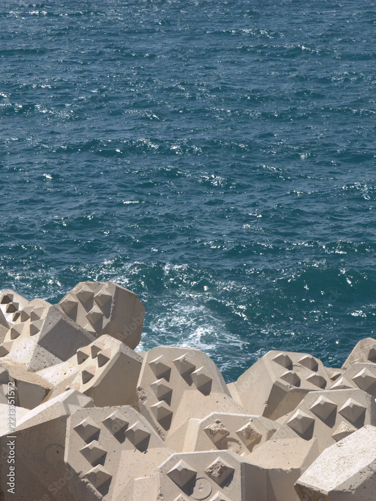 Fototapeta premium Concrete Tetrapod Breakwater Blocks Along Deep Blue Sea Coastline
