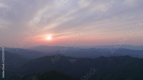 Early morning sun rises low on horizon in mountain landscape at dawn - aerial view