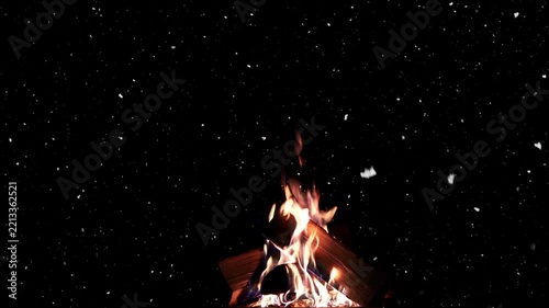 A campfire flickers as snow falls through the dark Christmas night, with space for text.