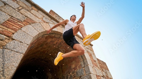 A dynamic young man leaping through the air over an ancient stone architectural structure.