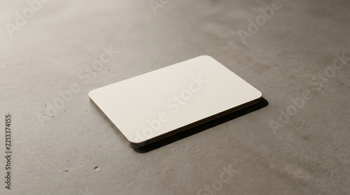 A blank off-white business card resting on a dark grey concrete surface with a sharp shadow cast to the right side of the in light isolated on a transparent background