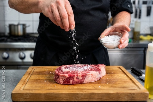 Chef Seasoning Raw Ribeye Steak on Wooden Cutting Board