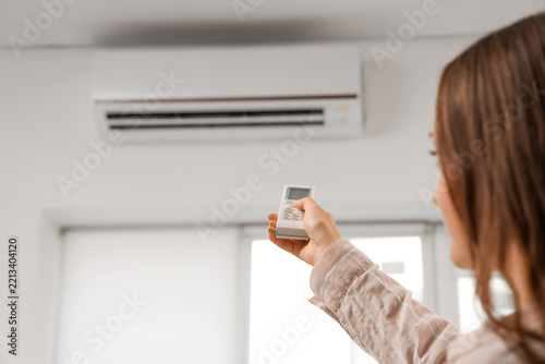 Climate control and energy efficiency, woman using remote to adjust air condi...