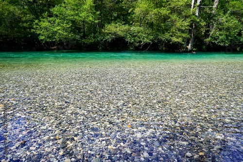 Crystal clear emerald green mountain river flowing over pebbles with lush green forest background in Kamikochi, Nagano, Japan