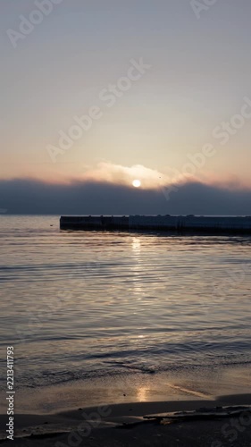 winter sea sunrise with sun glowing through fog vertical view, icy pier and calm ocean waves under golden morning sun, vertical view of misty winter sunset over sea with golden light path on water