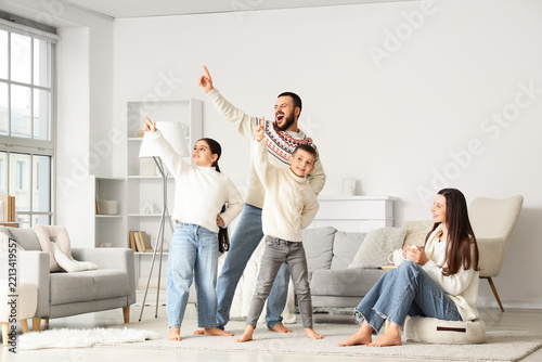 Happy parents with their little children in warm sweaters dancing at home on ...