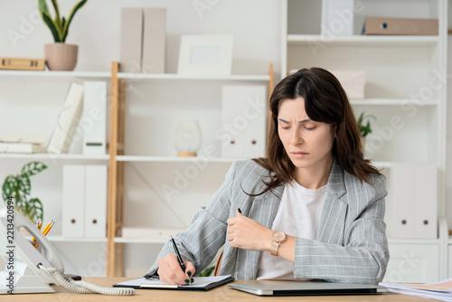 Work stress and deadline pressure, stressed woman checking time while writing...