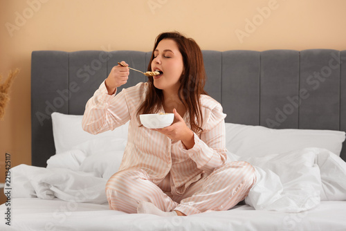 Self care and morning routine, woman in pajamas eating breakfast cereal in be...