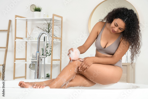 Self care and body hygiene, young woman washing legs with sponge and soap foa...