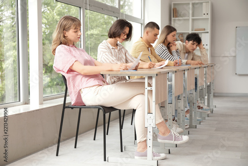 Academic testing and exam stress, diverse students sitting in a row at desks ...