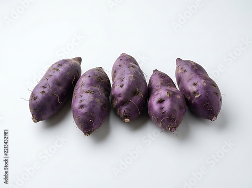 Five raw purple sweet potatoes arranged in a row isolated on white background