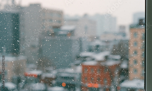 snowy cityscape seen through a window, soft falling snow, blurred urban background