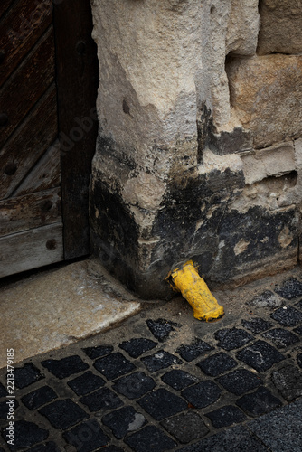 Bright Yellow Pipe Contrasting with an Old Weathered Wall, Cobblestone and Door. Close-up.