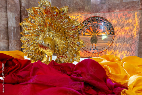 Gilded peacock statue decorated with gems and fanned feathers standing above red and yellow silk cloths inside the marble interior of the Quba Mere Diwane temple, Aknalich, Armenia
