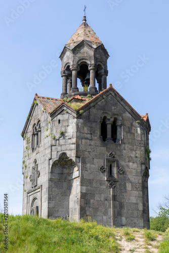 The stone bell tower of Haghpat Monastery topped with a cross rises against a vivid blue sky as a weathered medieval Armenian religious landmark and symbol, Haghpat, Armenia