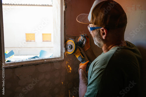 Worker cutting metal frame with angle grinder during renovation