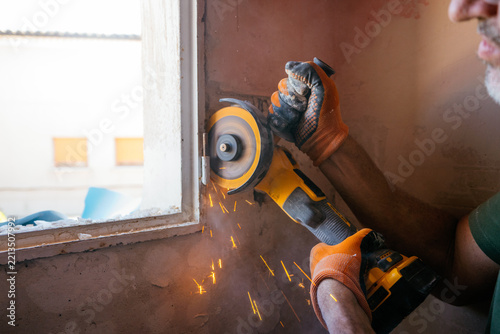 Worker using angle grinder cutting metal window frame