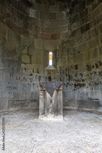 Stone altar stands inside the curved apse of an ancient orthodox church beneath a narrow window where soft light reveals old wall inscriptions, Eghegis, Armenia